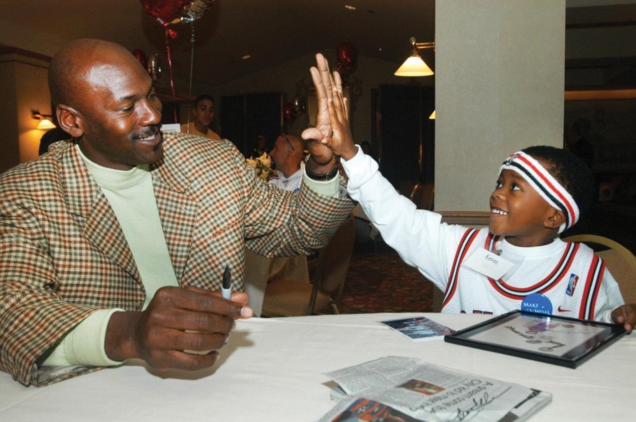 Michael Jordan high-fiving a young boy wearing a Make-A-Wish badge at a table